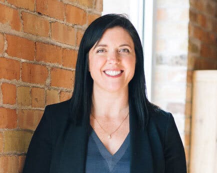 A photograph of a smiling person against a brick wall.