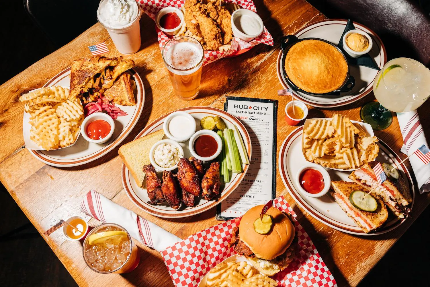 An aerial view of a table filled with various BBQ dishes, drinks, and a menu, indicating a late-night supper or gathering.