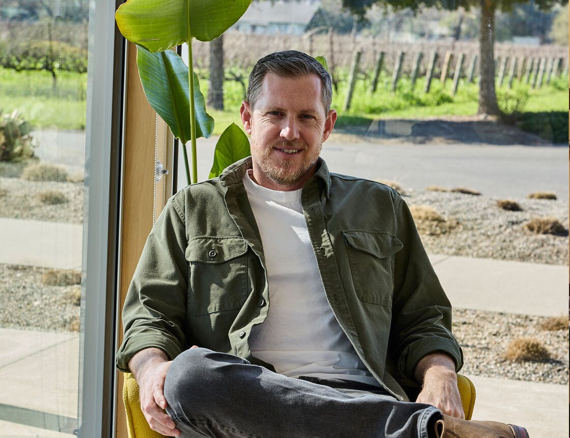 Person sitting down facing the camera with a vineyard in the background