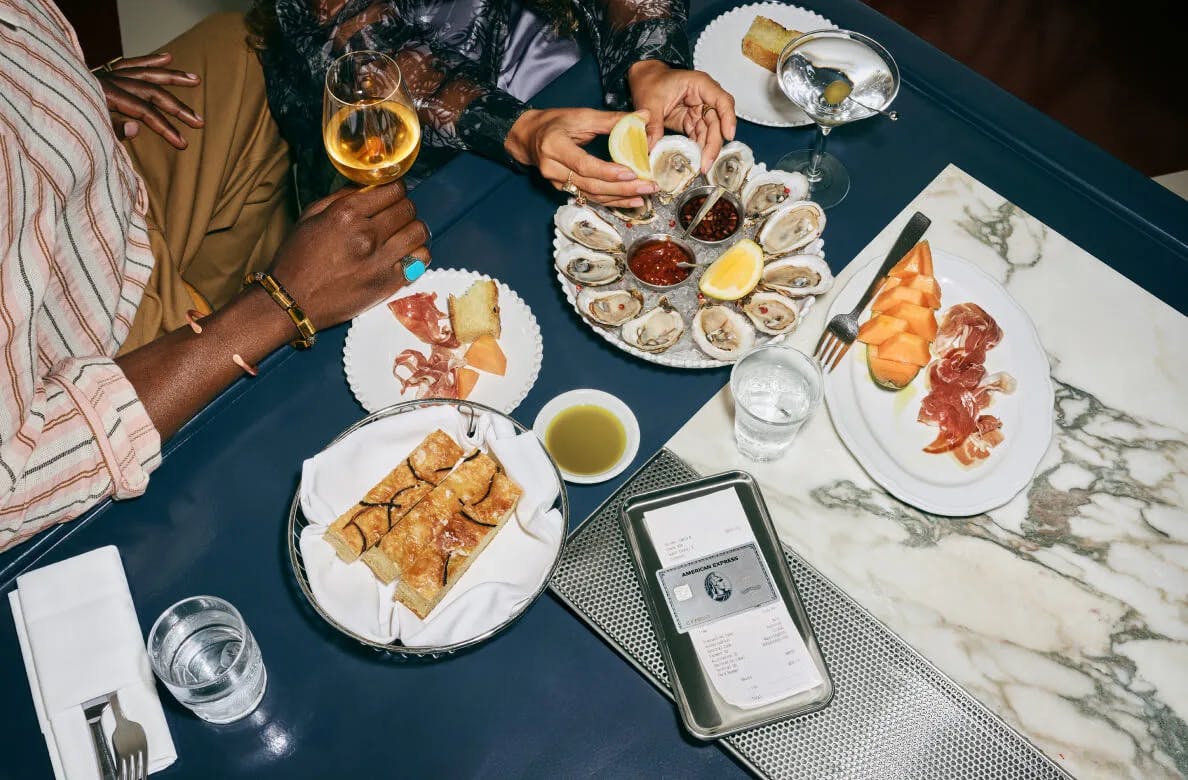 American Express credit card on a table with a glass of white wine, oysters and silverware in the background