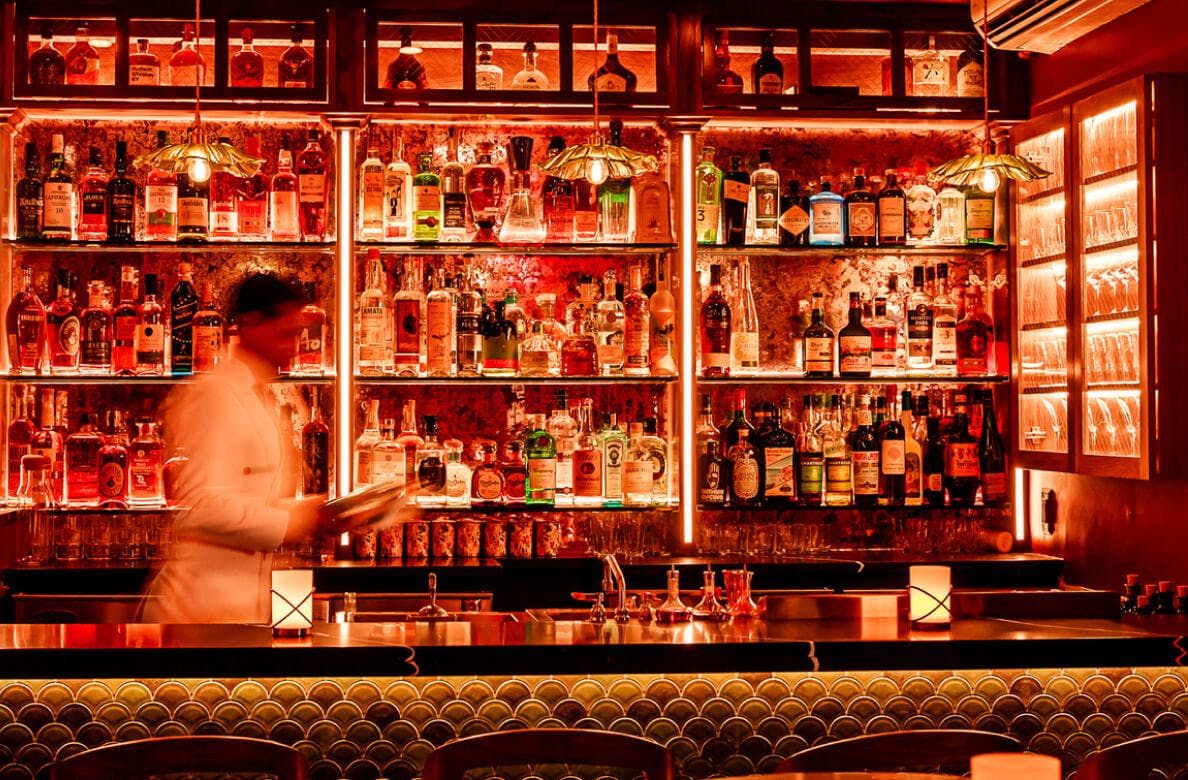 Intimately neon-lit bar with server setting up menus on the bar top