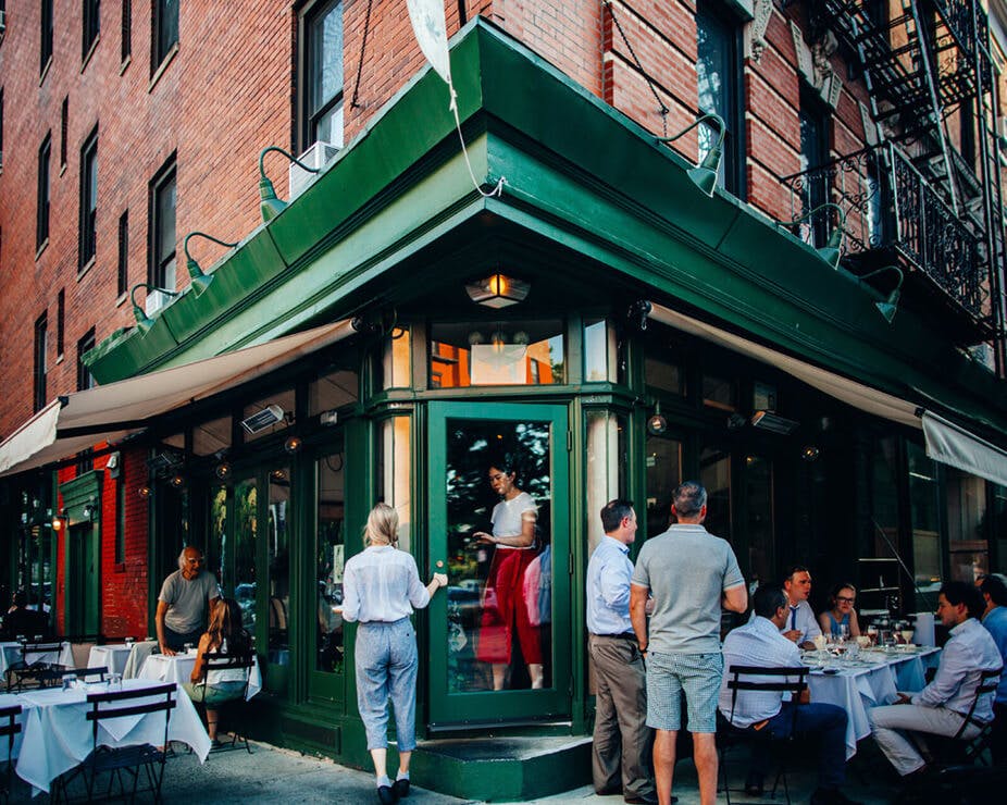 Restaurant exterior on a corner of a street with people dining al fresco under a green awning